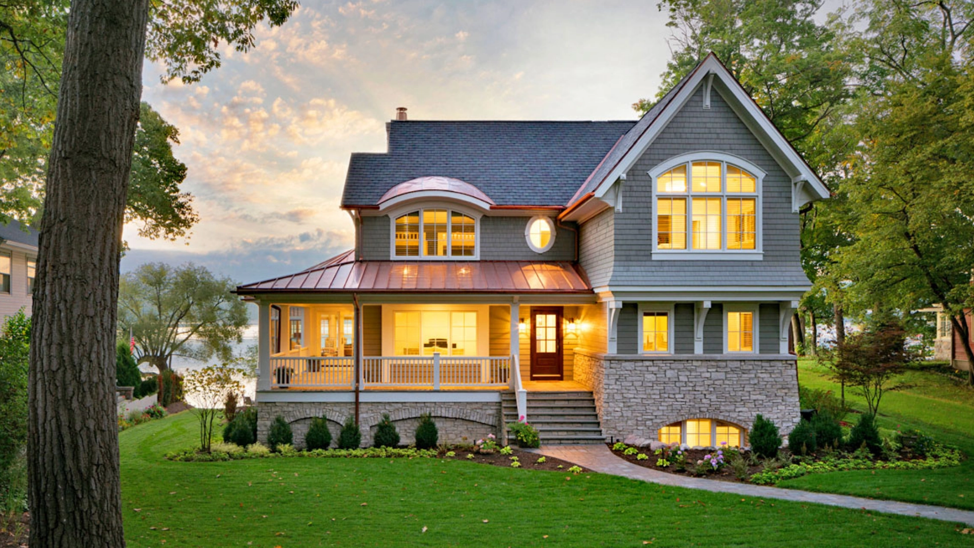 Elegant lakefront home with copper roof and stone facade at dusk