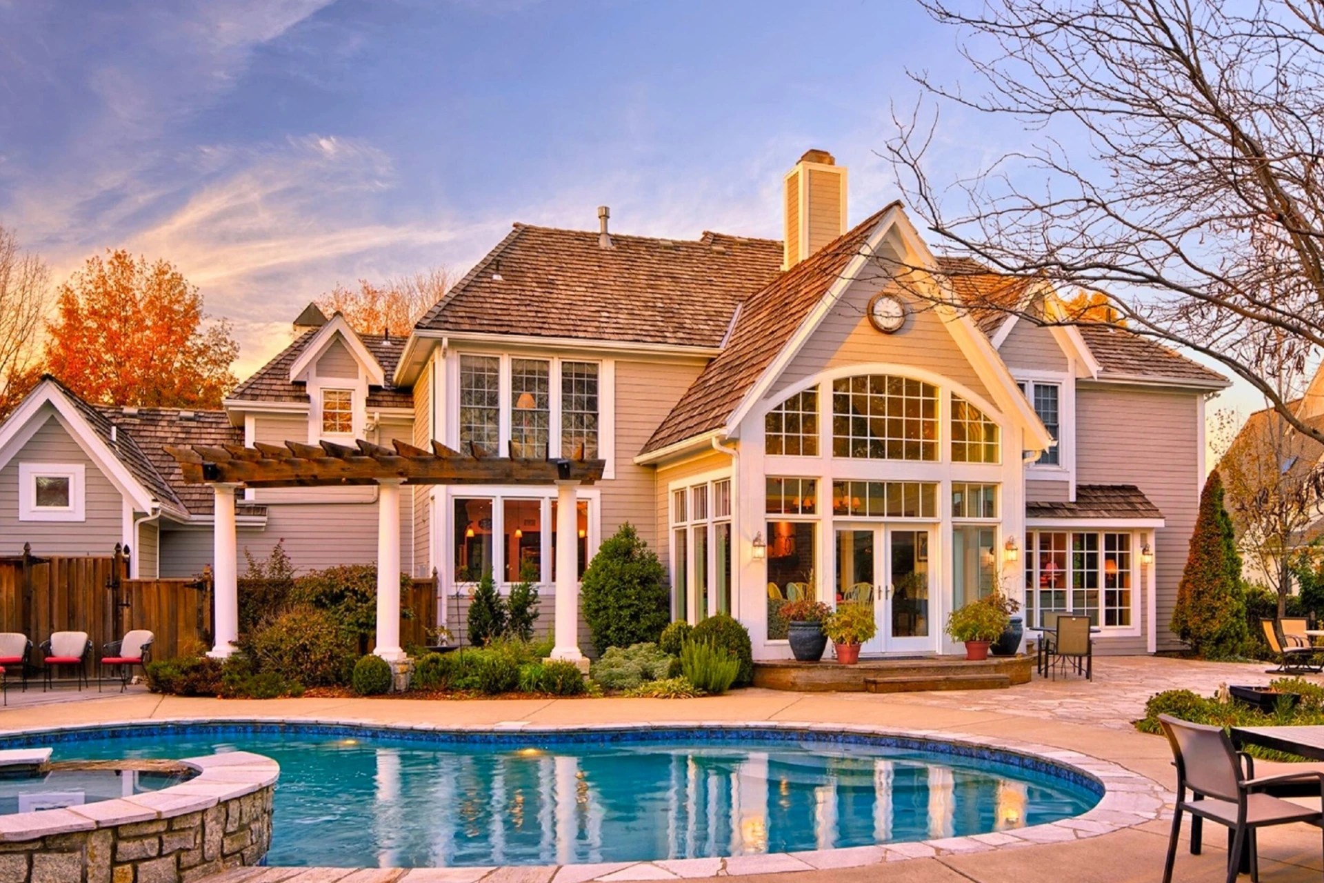 Twilight view of a shingle-style home with a curved pool and stone patio
