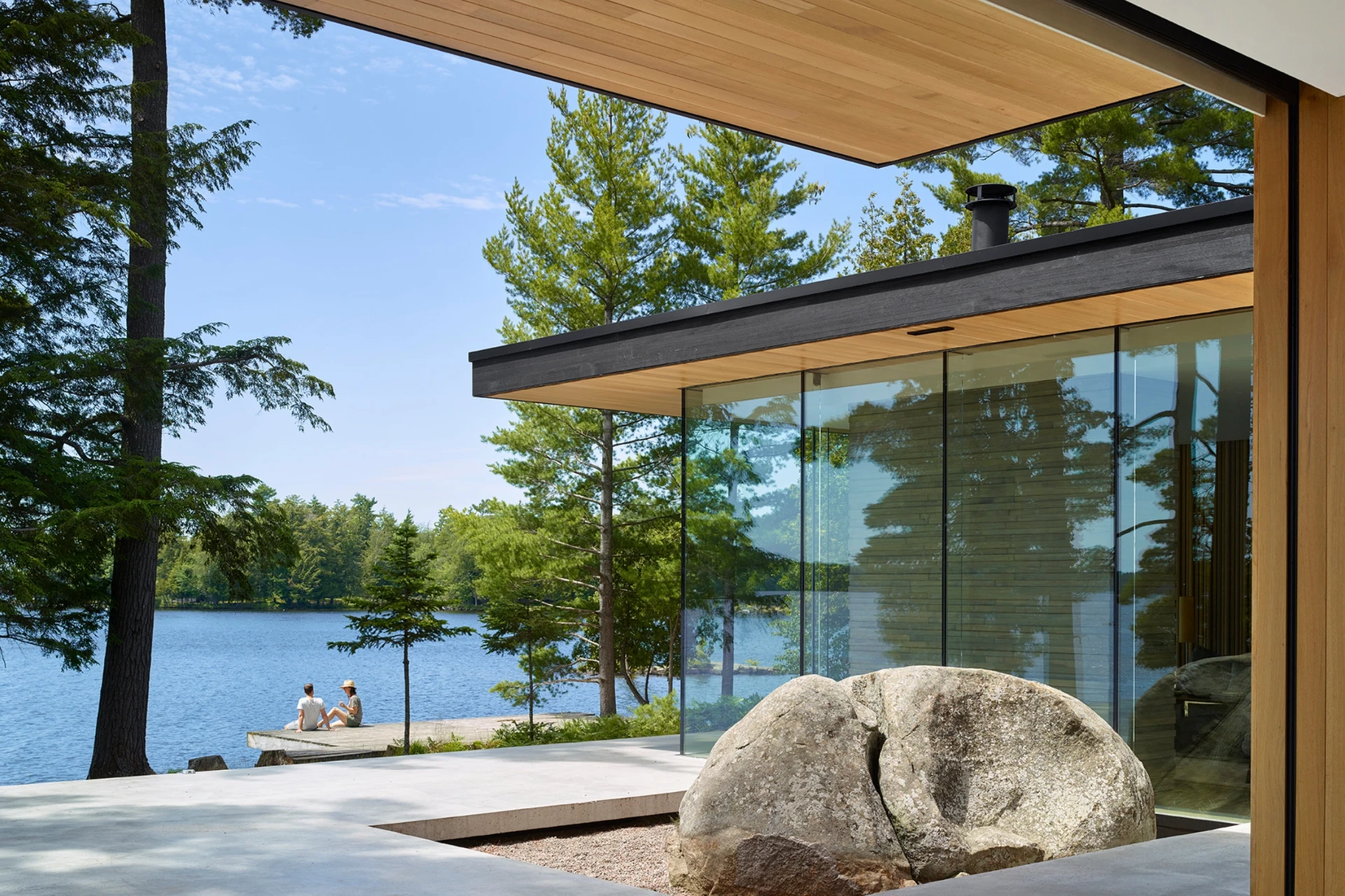 Modern glass and cedar lakeside home with a couple sitting on the dock beyond the terrace