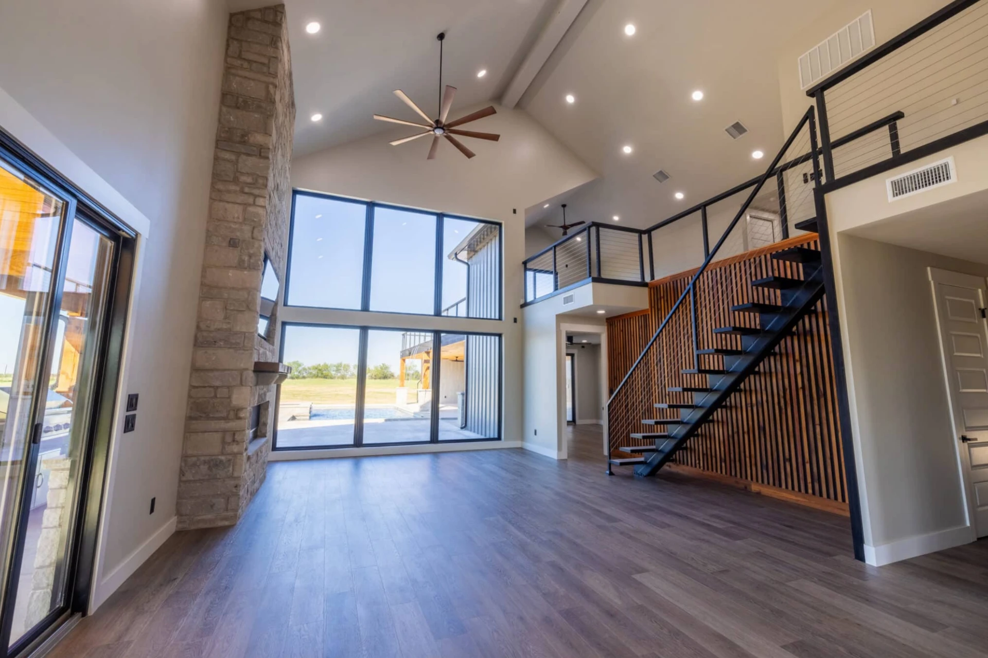 Open-concept new construction great room with vaulted ceiling, floor-to-ceiling windows, and floating steel staircase